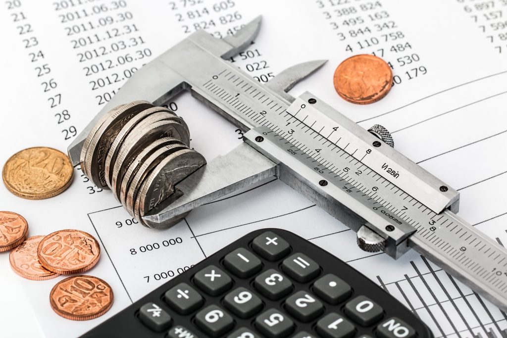 This image contains a leverage measuring money coins and a document where money spending is recorded.